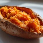 Close-up of a perfectly fluffy baked sweet potatoes, split open to show the bright orange interior.