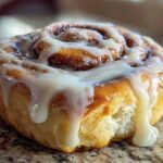 A close-up, mouthwatering shot of a freshly baked cinnamon roll topped with thick, dripping cream cheese icing.