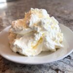 A generous dollop of light and fluffy cream cheese frosting piled high on a small white plate.