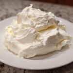 A generous mound of freshly whipped, bright white cream cheese frosting piled high on a white plate.