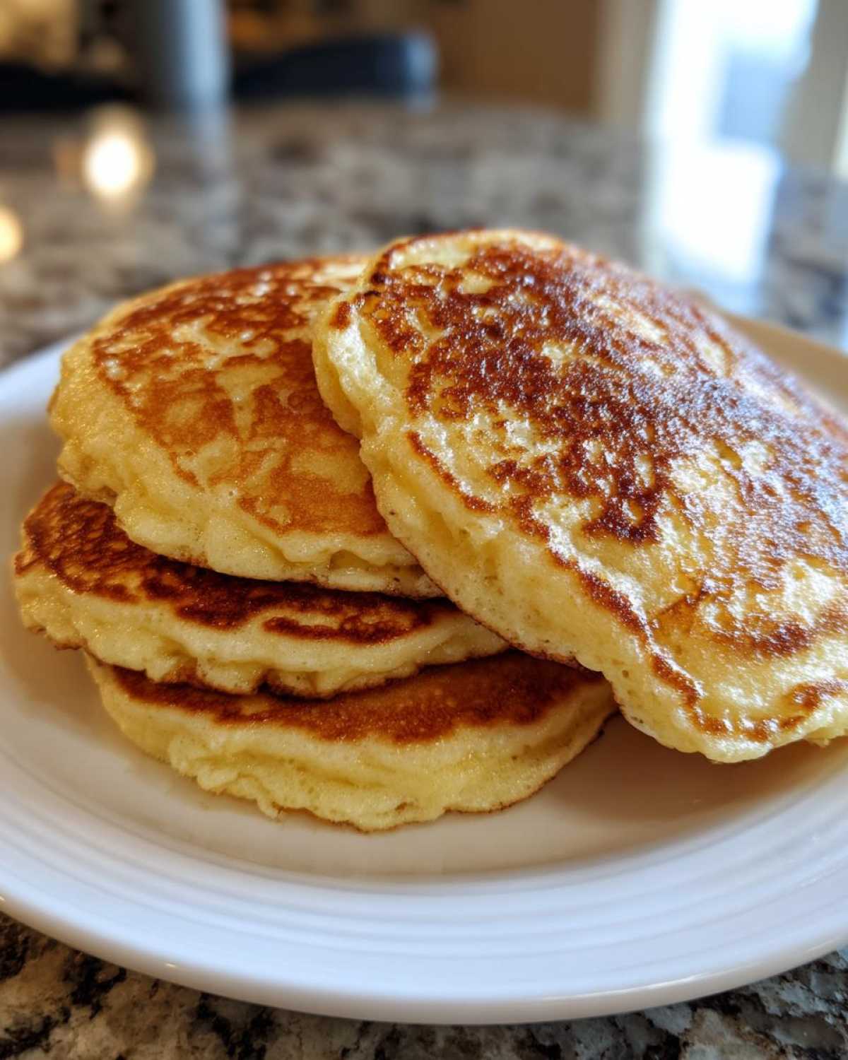 A close-up stack of three golden brown, thick, and fluffy pancakes served on a white plate.