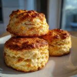 Three freshly baked, fluffy scones stacked slightly on a white plate, showing their golden crust.