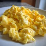 Close-up of perfectly cooked, fluffy scrambled eggs piled high on a white plate.