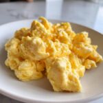 Close-up of incredibly fluffy, creamy scrambled eggs piled high on a white plate.