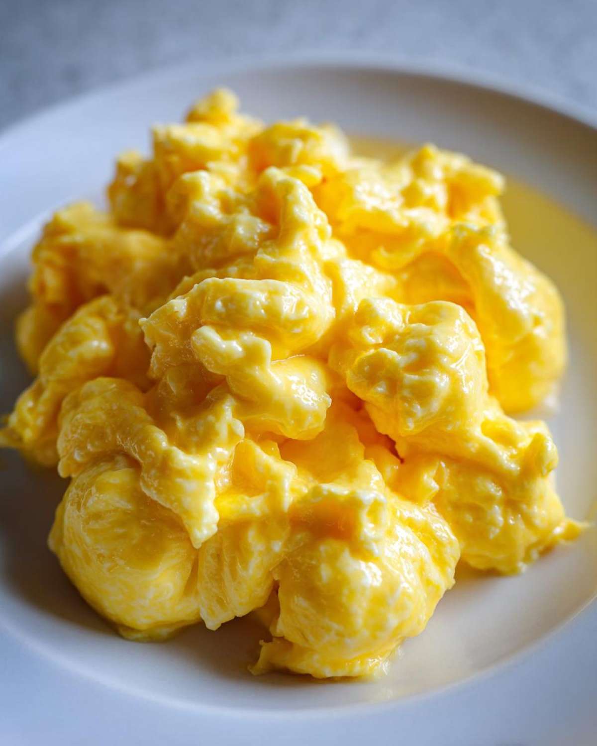 Close-up of perfectly cooked, fluffy scrambled eggs piled high on a white plate.