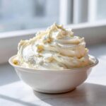 A generous mound of fluffy, pale yellow vanilla buttercream frosting piled high in a white bowl.