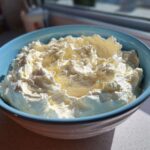 A bright blue bowl filled with freshly whipped, fluffy vanilla buttercream frosting, catching the sunlight.
