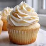 Close-up of a fluffy vanilla cupcake topped with a tall swirl of white vanilla buttercream frosting.