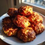 A stack of freshly baked, golden brown cream cheese sausage balls piled high on a white plate.