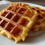 Close-up of two golden brown, fluffy high protein waffles stacked slightly on a white plate.