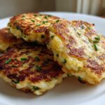 A stack of four golden brown, pan-fried mashed potato cakes garnished with fresh green chives on a white plate.