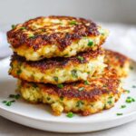 A stack of three golden brown, pan-fried mashed potato cakes garnished with fresh chives.