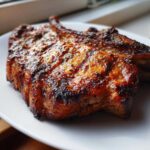 Close-up of a thick, juicy, grilled pork chop showing char marks and a rich glaze from the marinade for pork chops.