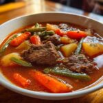 Close-up of a steaming bowl of rich vegetable beef soup featuring tender beef chunks, carrots, potatoes, and green beans.