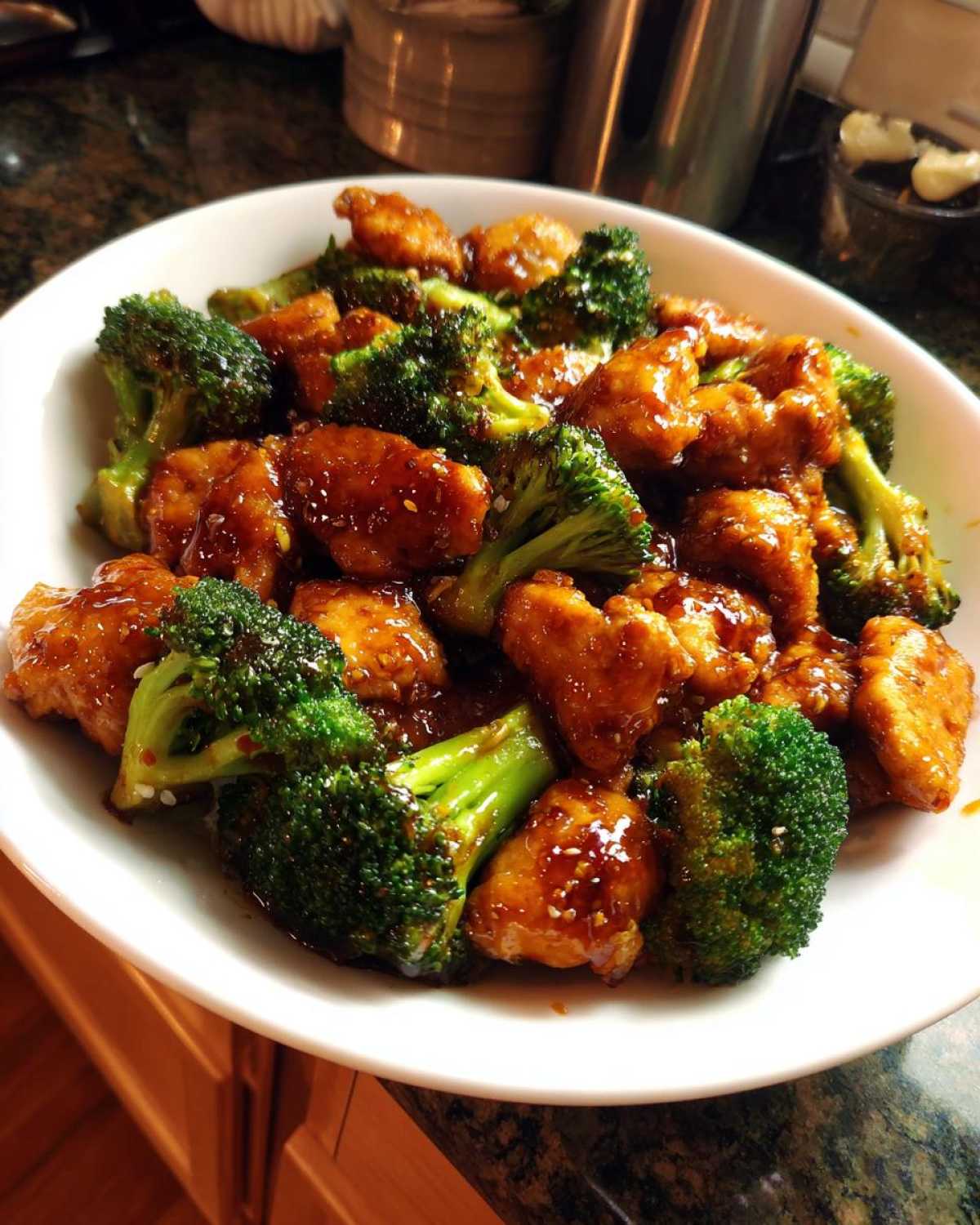 Close-up of glossy, saucy honey garlic chicken and broccoli served in a white bowl.
