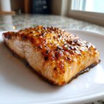 Close-up of a perfectly cooked, glazed honey garlic salmon fillet resting on a white plate.