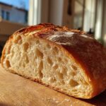 Close-up of a freshly baked Italian bread loaf, showing the open, airy crumb structure and golden crust.