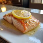 Close-up of a perfectly cooked piece of baked salmon recipe topped with a lemon slice and butter sauce.