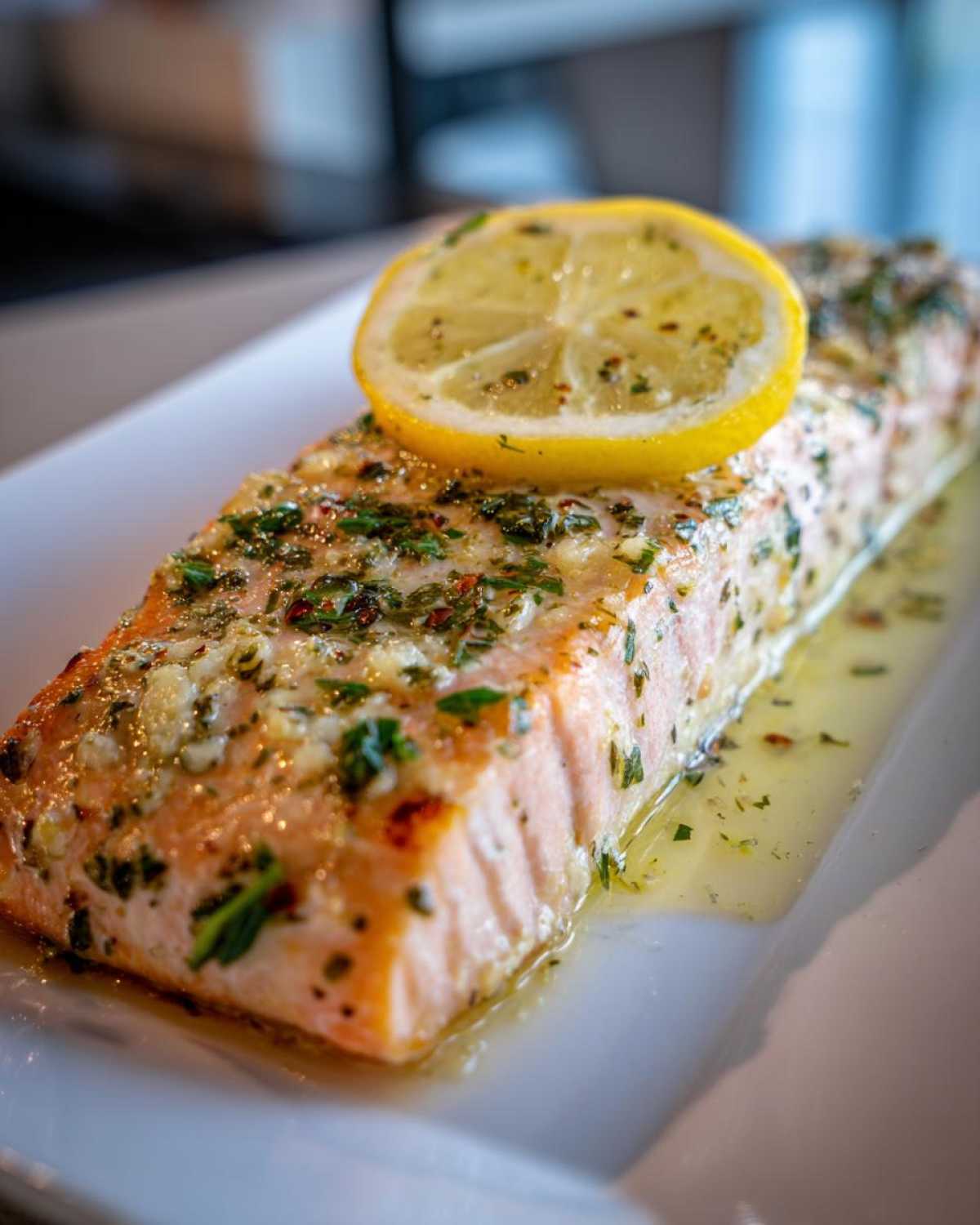 Close-up of a perfectly cooked baked salmon recipe fillet topped with herbs, garlic, and a slice of fresh lemon.