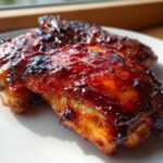 Close-up of two juicy bbq chicken wings covered in a thick, glossy, caramelized sauce on a white plate.
