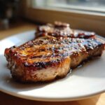 Close-up of a juicy, glazed pork steak recipe cooked perfectly, resting on a white plate.