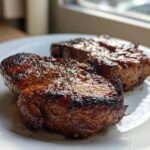 Two perfectly seared and glazed pork steak cuts resting on a white plate, showcasing a rich brown crust.