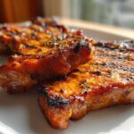Close-up of two glazed, grilled pork chops seasoned with herbs, showing the results of the best marinade for pork chops.