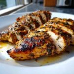 Close-up of perfectly cooked and sliced greek chicken breast, glistening with marinade and herbs.