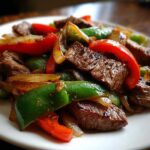 Close-up of sizzling steak fajitas featuring seared beef strips, green bell peppers, and red peppers.