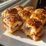 Close-up of freshly baked Ham and Cheese Sliders with melted cheese oozing out, topped with everything bagel seasoning.