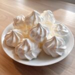 A plate piled high with freshly piped, bright white meringue cookies with distinct swirls.