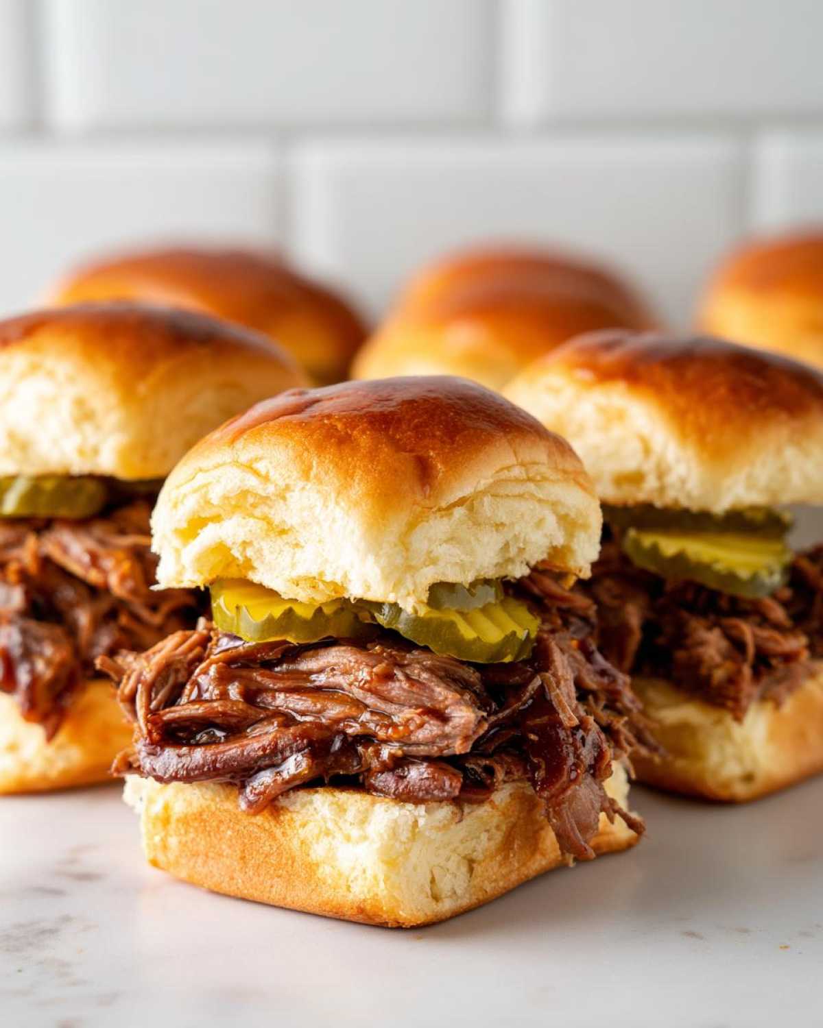 A close-up of delicious mississippi pot roast sliders piled high with shredded beef and pickles on soft slider buns.