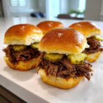 Four glistening mississippi pot roast sliders piled high with shredded beef and pickle slices on brioche buns.