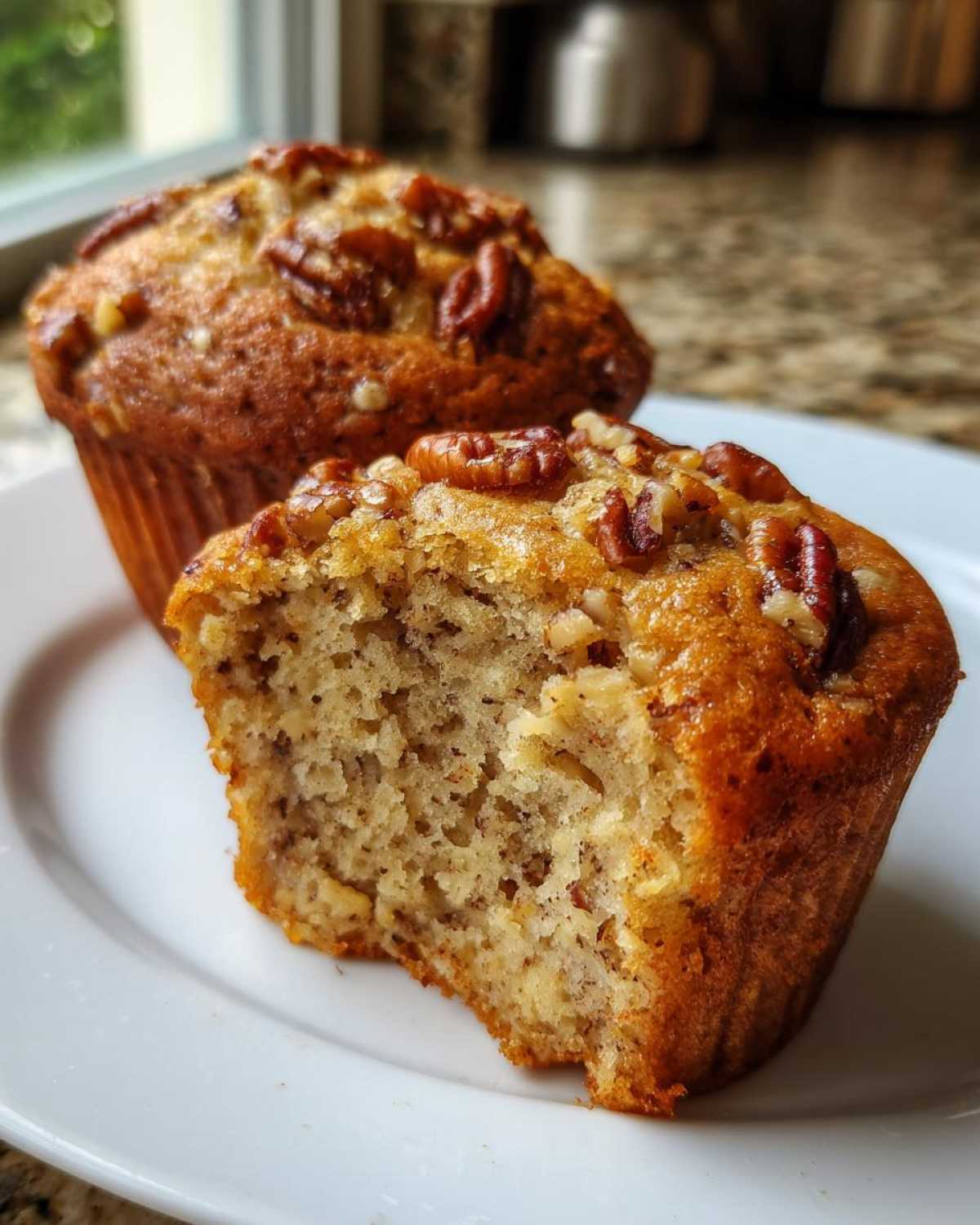 Close-up of a moist banana nut muffin, one half-eaten to show the soft interior and pecan topping.