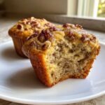 Close-up of a banana nut muffin with a bite taken out, showing the moist interior and pecan topping.