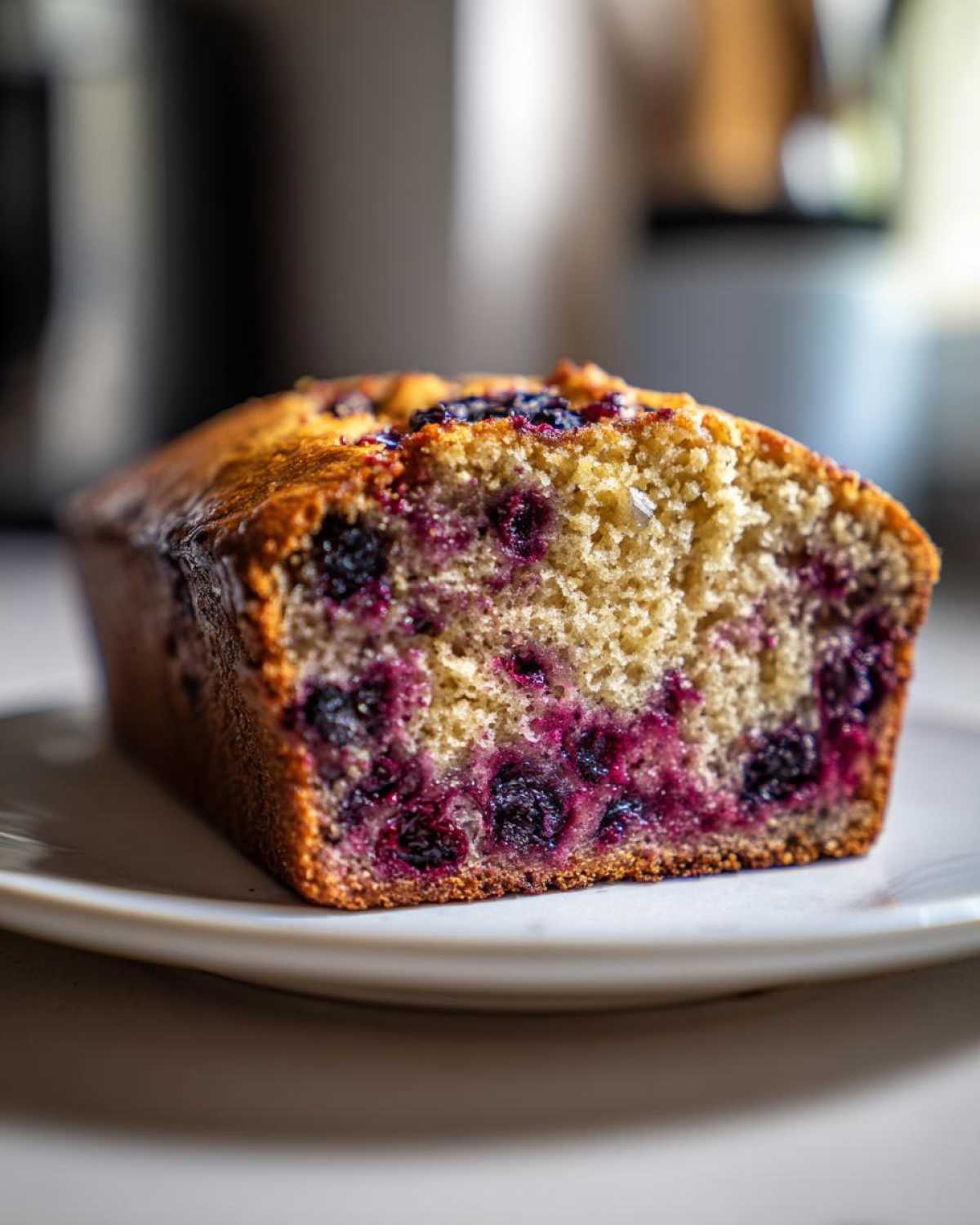 Close-up of a slice of moist blueberry banana bread showing the rich purple blueberries baked into the golden crumb.