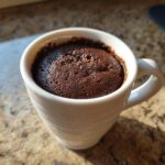 Close-up of a freshly baked, moist chocolate mug cake filling a white ceramic mug.