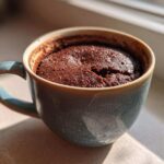 Close-up of a freshly baked, moist chocolate mug cake filling a speckled blue ceramic mug.