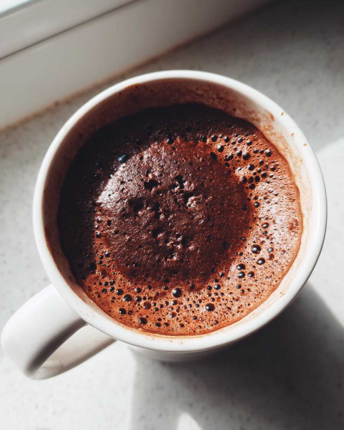 Overhead view of a freshly baked chocolate mug cake with a bubbly, moist top in a white mug.