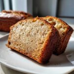 Two thick slices of moist sugar free banana bread showing a golden crust and speckled interior.