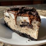 A decadent slice of no-bake Oreo pie featuring a dark crust, creamy filling with cookie chunks, whipped topping, and chocolate drizzle.