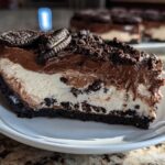 A thick slice of no-bake Oreo pie showing dark crust, white cream layer, and chocolate mousse topping, garnished with Oreo cookies.