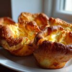 Close-up of four golden brown, perfectly risen yorkshire pudding cups on a white plate.