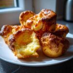 A close-up of several golden brown, perfectly risen yorkshire pudding piled on a white plate.