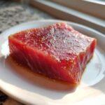 Close-up of a thick, vibrant red raw tuna steak coated lightly in spices, resting in a pool of liquid from the MARINADE FOR TUNA STEAK.