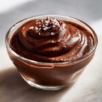 Close-up of rich homemade chocolate pudding swirled in a glass dish, topped with flaky sea salt.