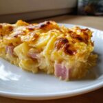 A close-up of a cheesy, baked slice of scalloped potatoes and ham on a white plate.