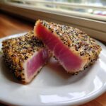 Two halves of perfectly seared ahi tuna, showing a bright pink, rare center and a thick sesame seed crust.