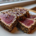 Four slices of perfectly Seared Ahi Tuna, crusted with sesame seeds and pepper, showing a bright red center.