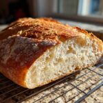 Close-up of a freshly baked loaf of soft French bread, cut open to show the airy crumb and golden crust.
